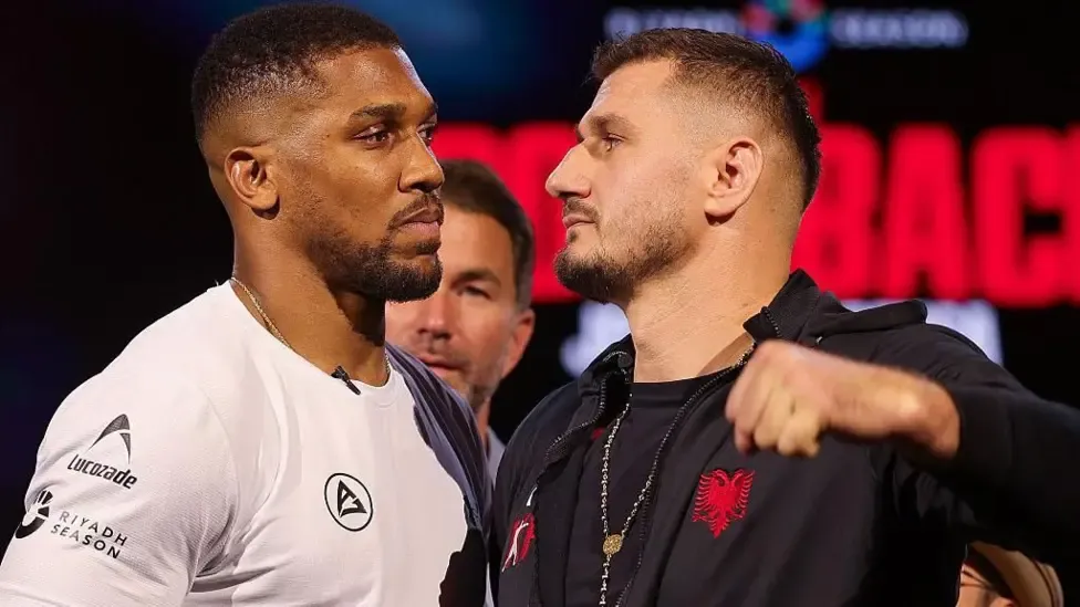 Anthony Joshua and Kristian Prenga face off as they look each other in the eye, Joshua wearing a white top and Prenga in a black hoodie